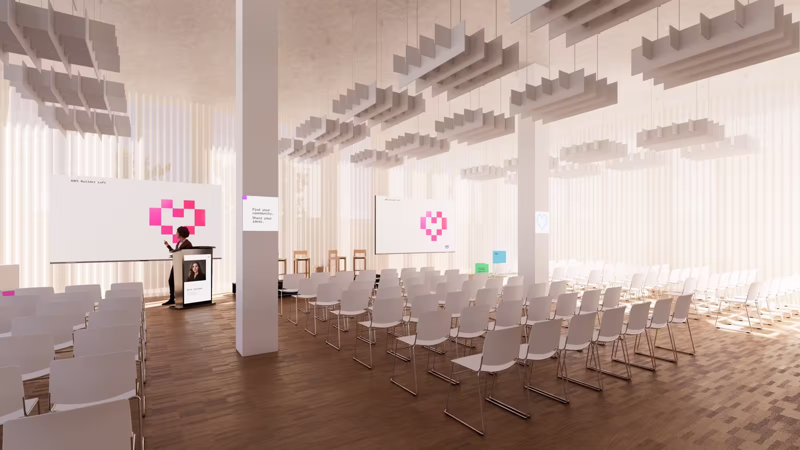3D rendering of an AWS Builder Loft event space configured for a keynote or community talk. Rows of white chairs face a podium where a speaker stands beside a screen displaying the AWS Builder Loft pixel-heart logo in pink. A second screen reads "Find your community. Share your ideas." The space features warm wood flooring, floor-to-ceiling sheer curtains letting in soft natural light, and sculptural geometric ceiling installations made of stacked cube forms. The atmosphere is modern, airy, and community-focused.